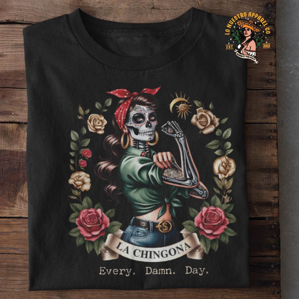 La Chingona, Every Damn Day, folded on a wooden table showcasing Lo Nuestro Apparel's funny shirts and Chicano Clothing line.