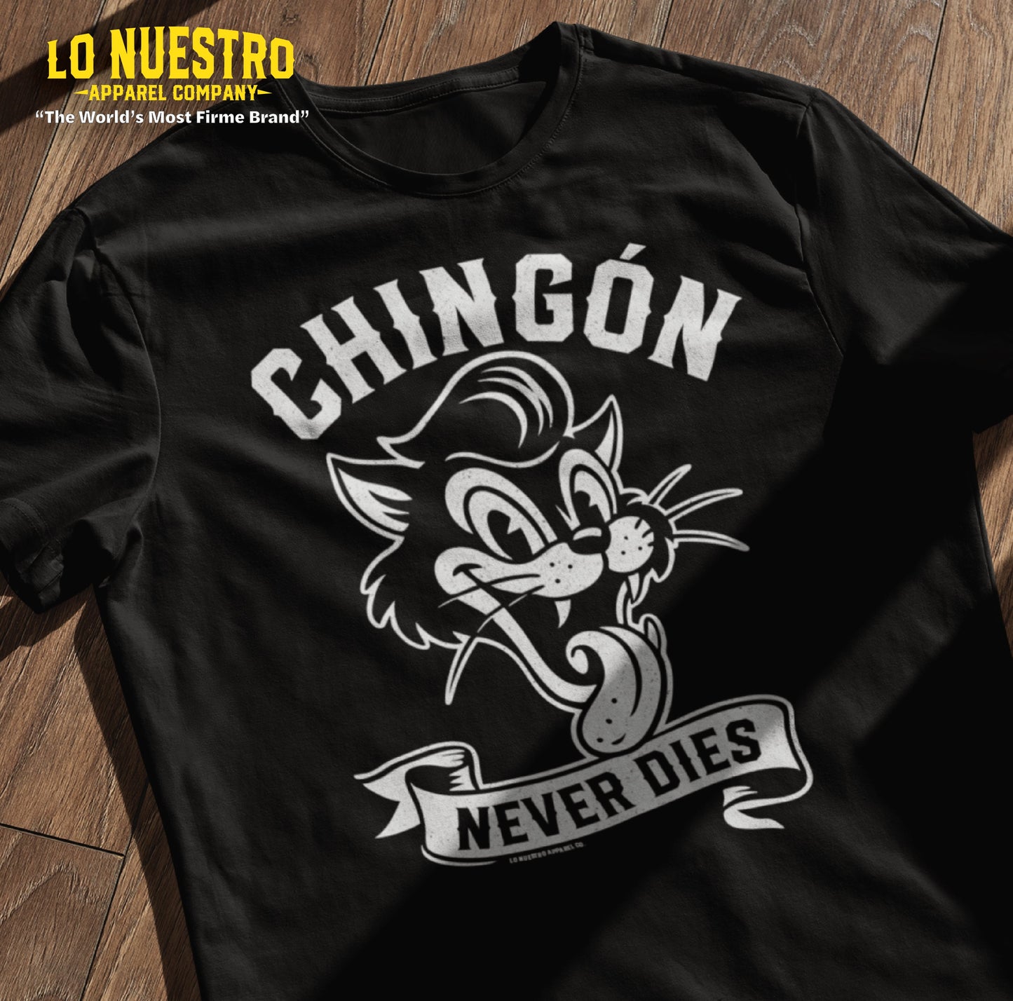 Black Chingon Never Dies t-shirt featuring a rockabilly cartoon cat, laid flat on a wooden surface with natural lighting. Funny Mexican Shirt.