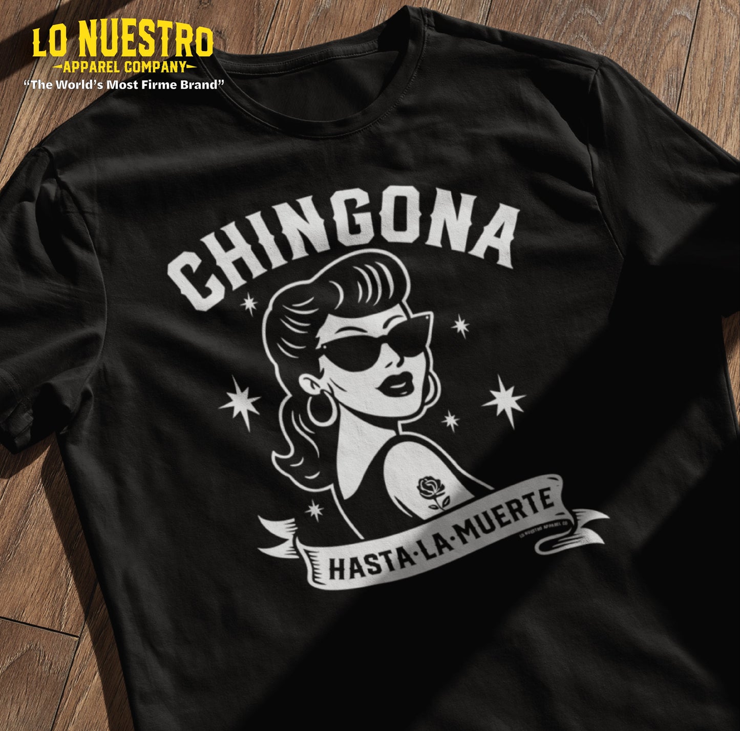 Flatlay of a black Chicana shirt featuring a retro rockabilly girl and Chingona Hasta La Muerte text, designed for bold Latina style.