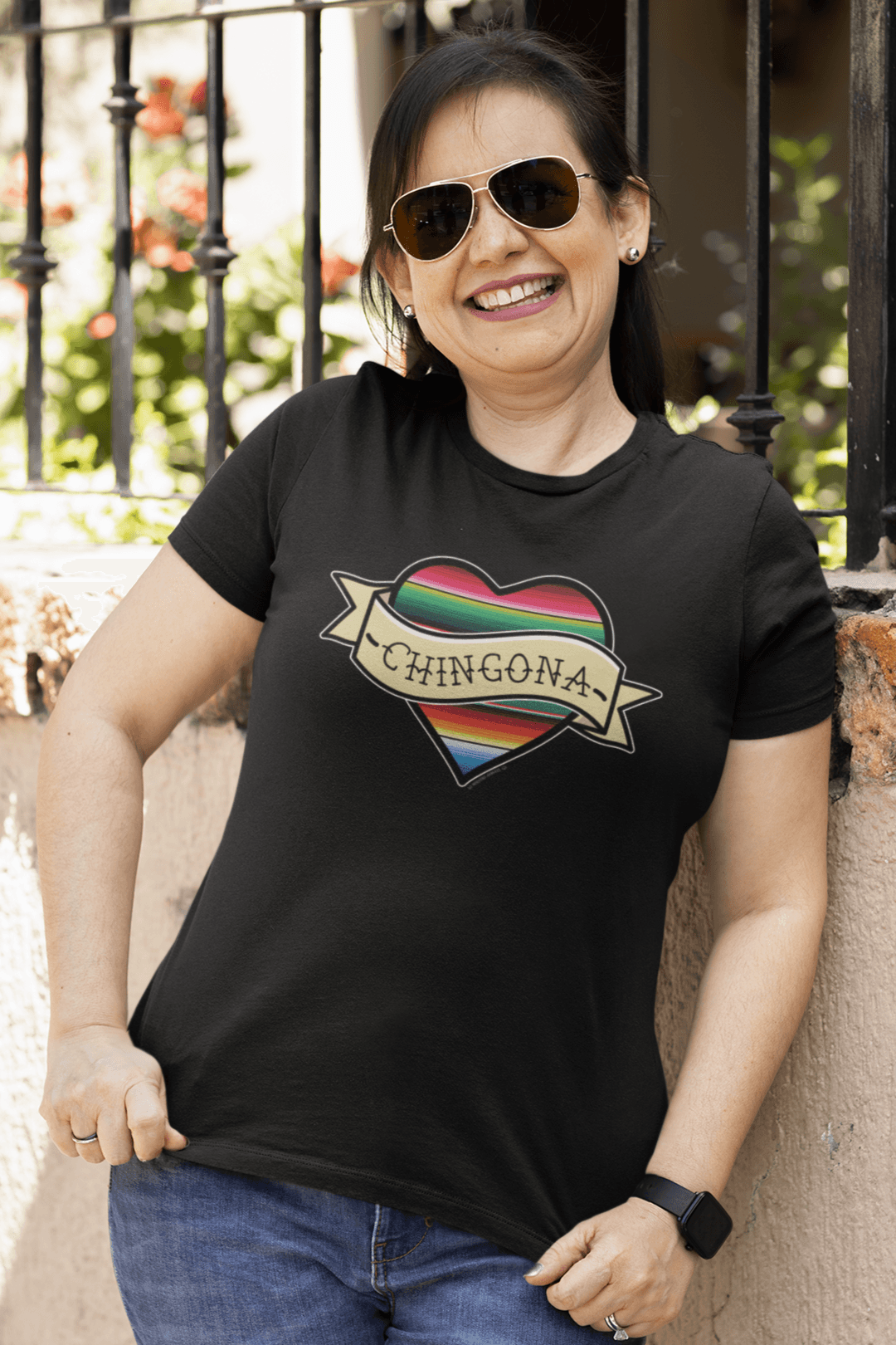 Woman wearing a Chingona serape heart t-shirt, standing outdoors and smiling.