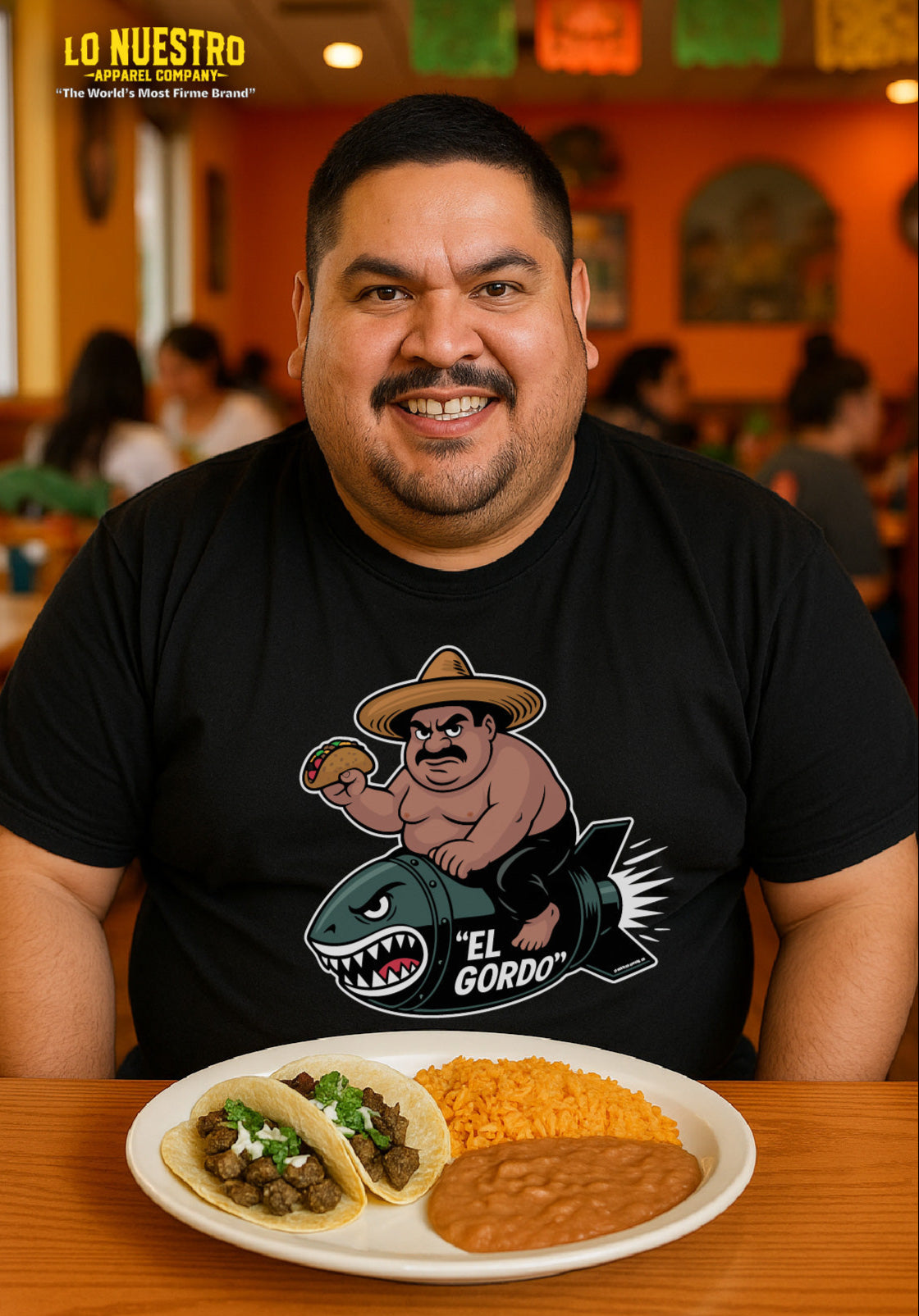 A smiling Hispanic man wearing a plain black t-shirt sitting at a table in a Mexican restaurant with two carne asada tacos, rice, and beans on a plate in front of him.