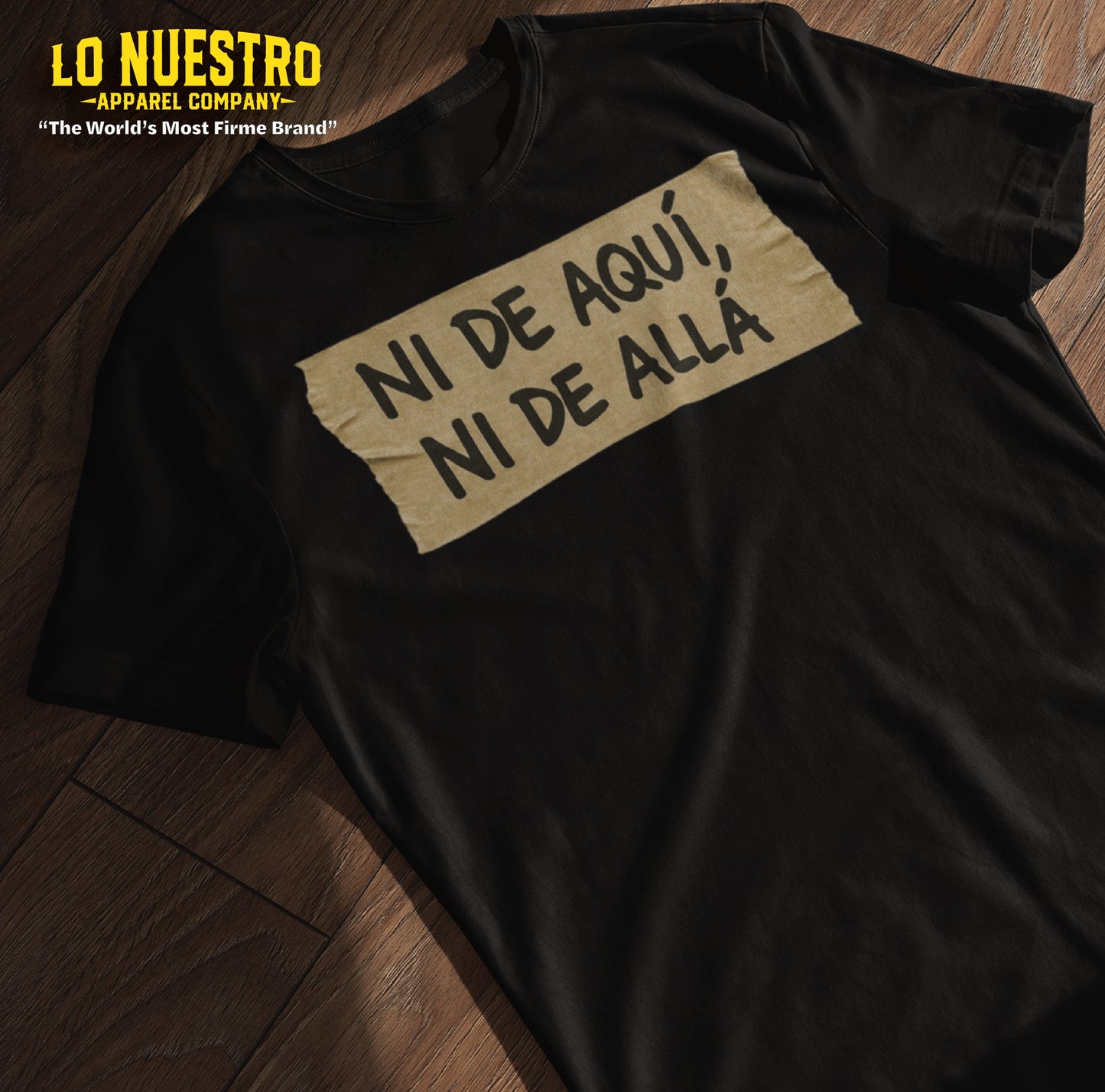 Flatlay of a funny Mexican shirt on wood floor with masking tape graphic that says Ni de aquí, ni de allz