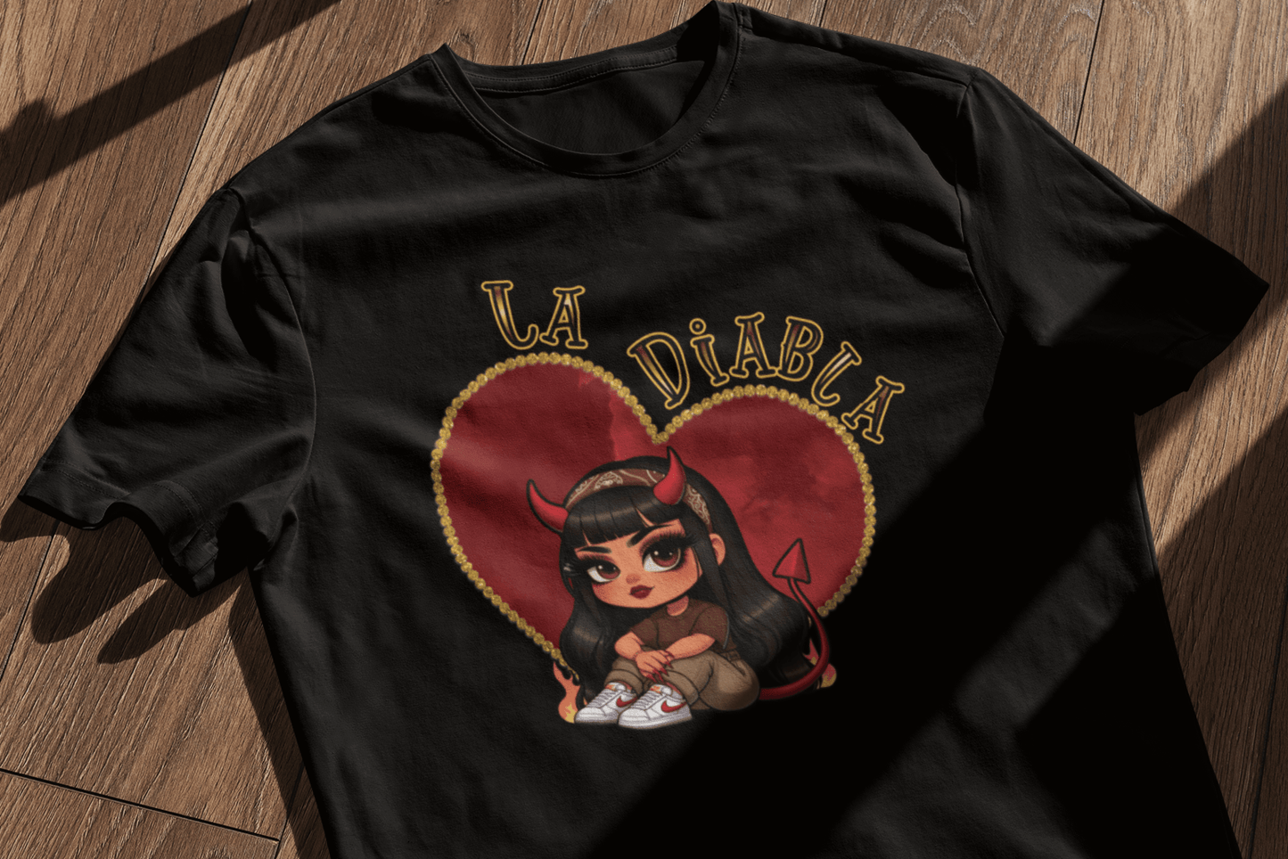 La Diabla black t-shirt laid on a wooden surface, featuring a cute devil girl inside a heart design—perfect for Chicana fashion and Valentine's Day outfits