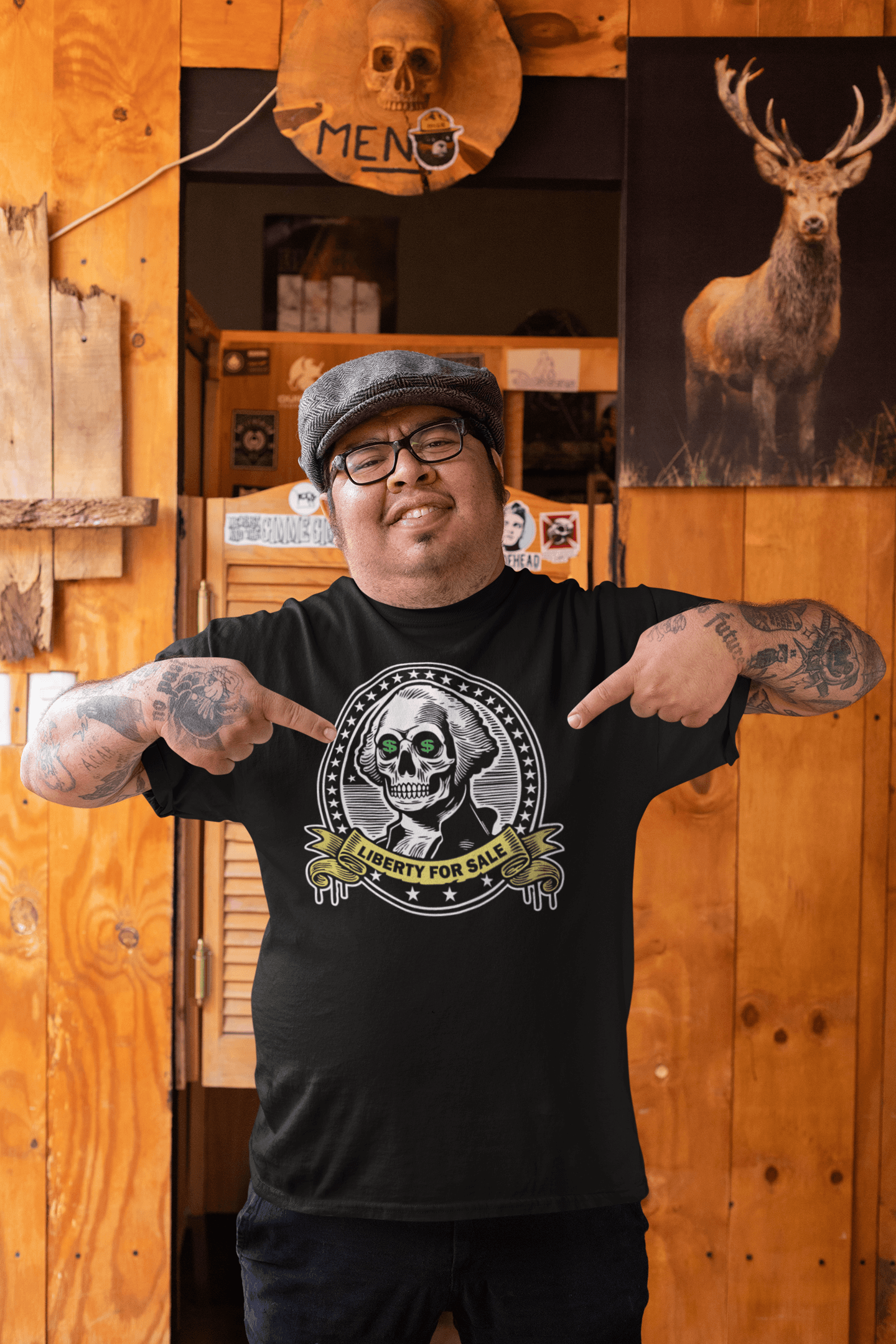 Man wearing the 'Liberty for Sale' t-shirt, featuring a skeletal George Washington with dollar signs in his eyes, standing in a rustic bar environment and proudly pointing at his shirt.