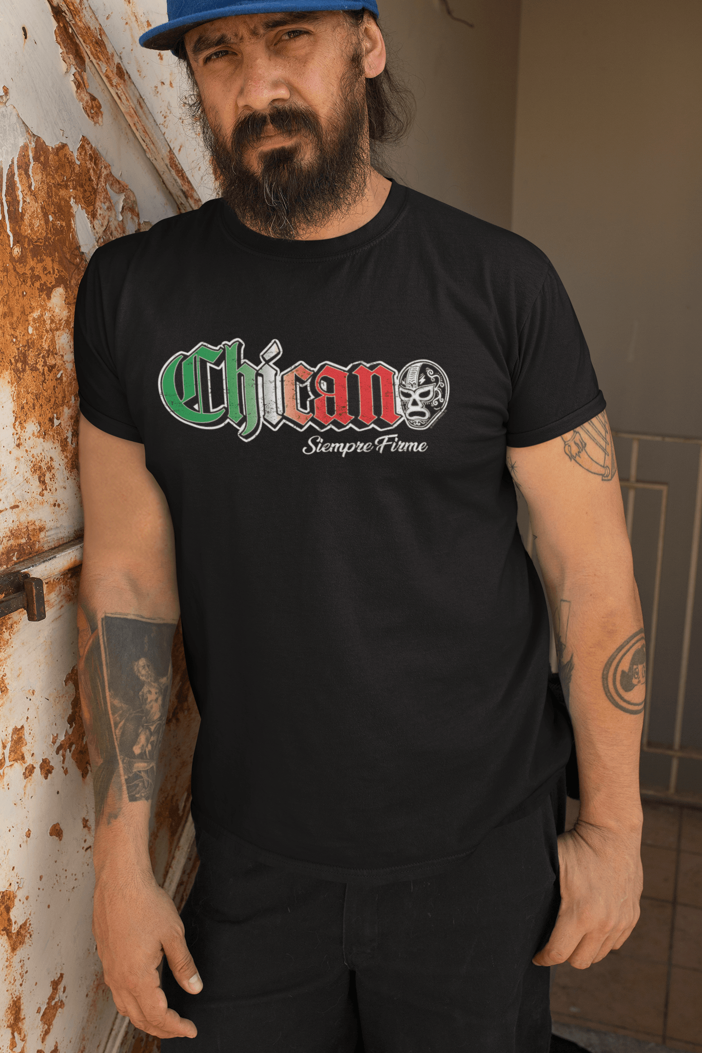 Man wearing Chicano Siempre Firme T-Shirt in Black, with a bold graphic featuring Mexican flag colors and 'Siempre Firme' text below, standing against a rusty wall.