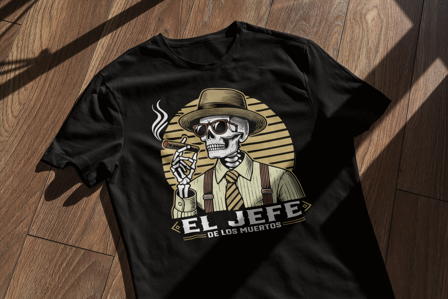 Close-up mockup of the 'El Jefe de los Muertos' t-shirt laid on a wooden surface, with a window shadow casting over it, showing the skeleton design with a fedora and cigar."