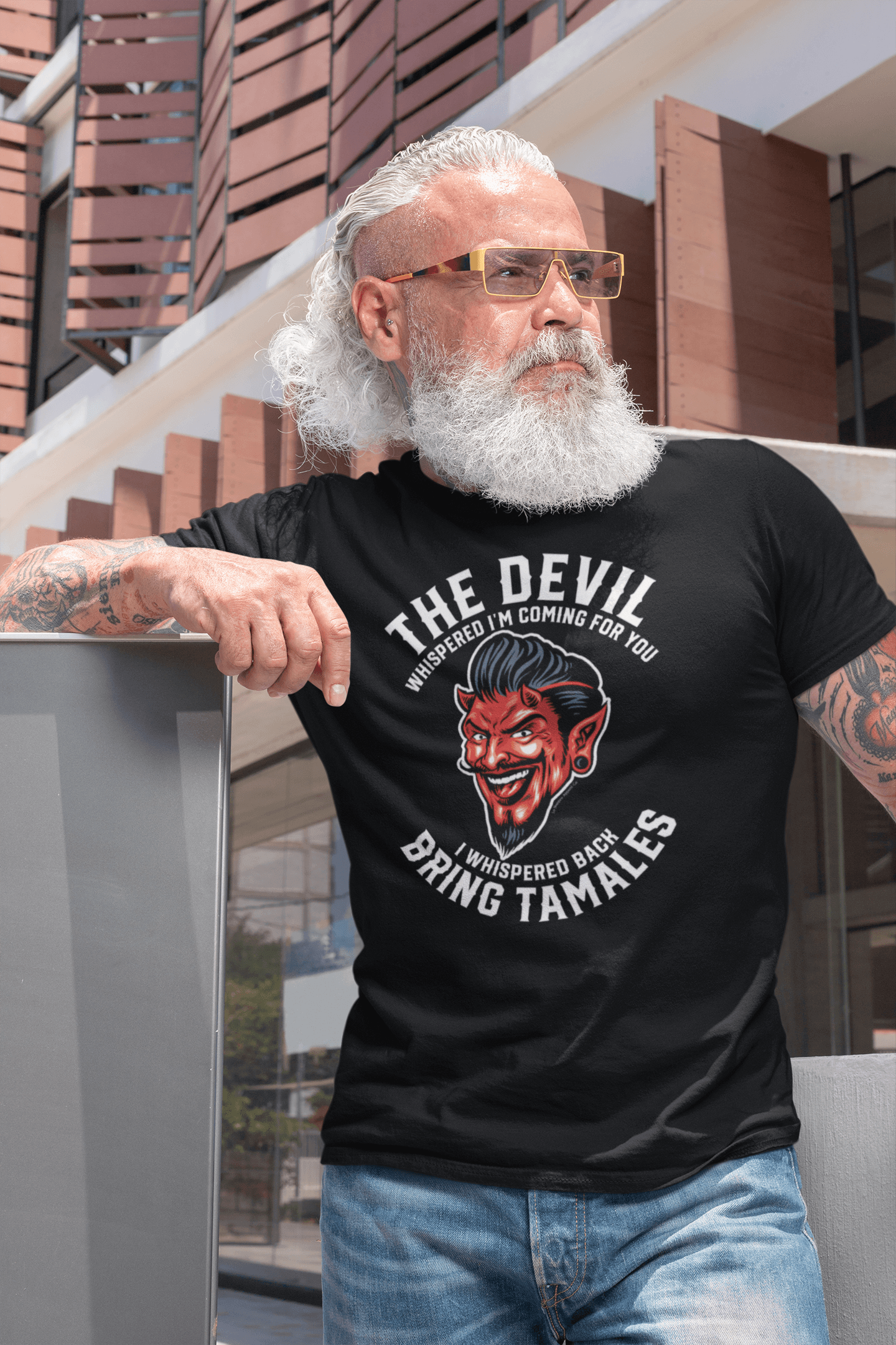A trendy middle-aged man with sunglasses wearing a black t-shirt with a devil graphic and the text 'The Devil Whispered I'm Coming For You. I Whispered Back Bring Tamales.