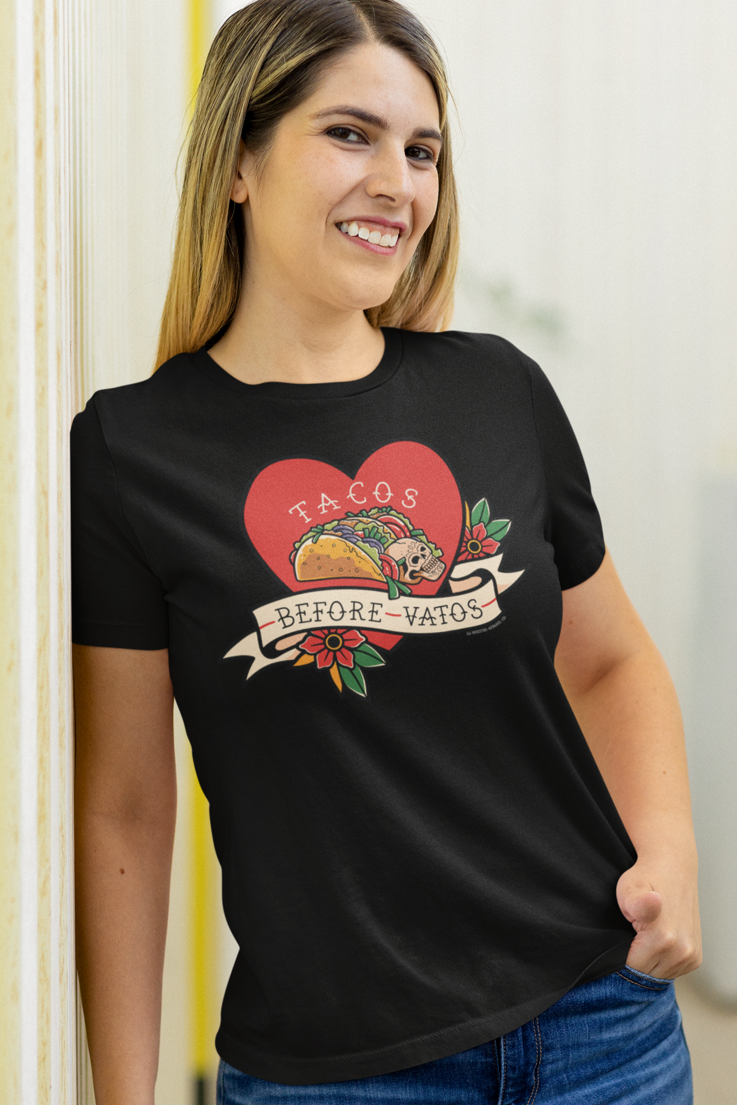 Smiling woman wearing a black "Tacos Before Vatos" T-shirt with a heart and taco graphic. Fun and stylish women's taco-themed tee.