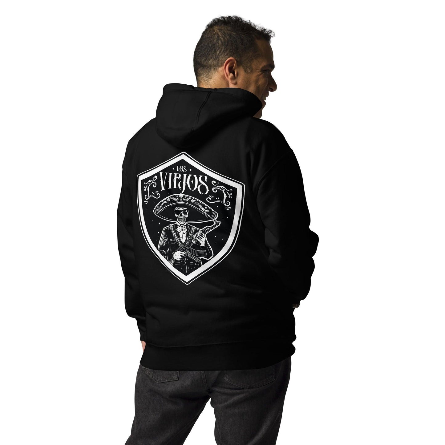 Man wearing a black hoodie with the back design of a charro skeleton and “Los Viejos” text, standing in an indoor space.