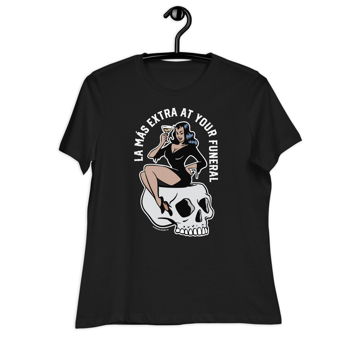 Black t-shirt on a hanger featuring the design of a pin-up woman sitting on a skull with a martini, paired with the text “La Más Extra at Your Funeral.