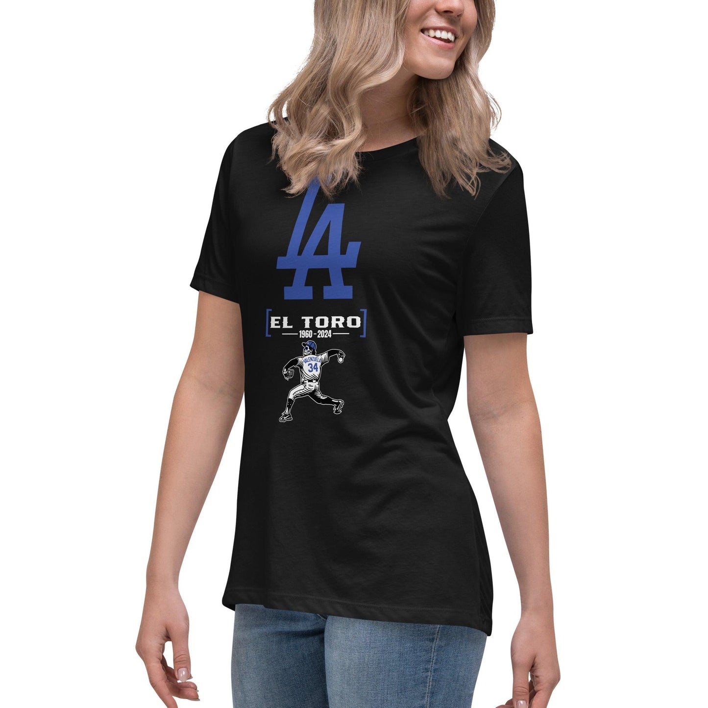 Woman wearing a black El Toro t-shirt with a large blue LA logo and an illustration of a baseball player in a pitching motion. The t-shirt tribute features 'El Toro 1960-2024' text below the logo.