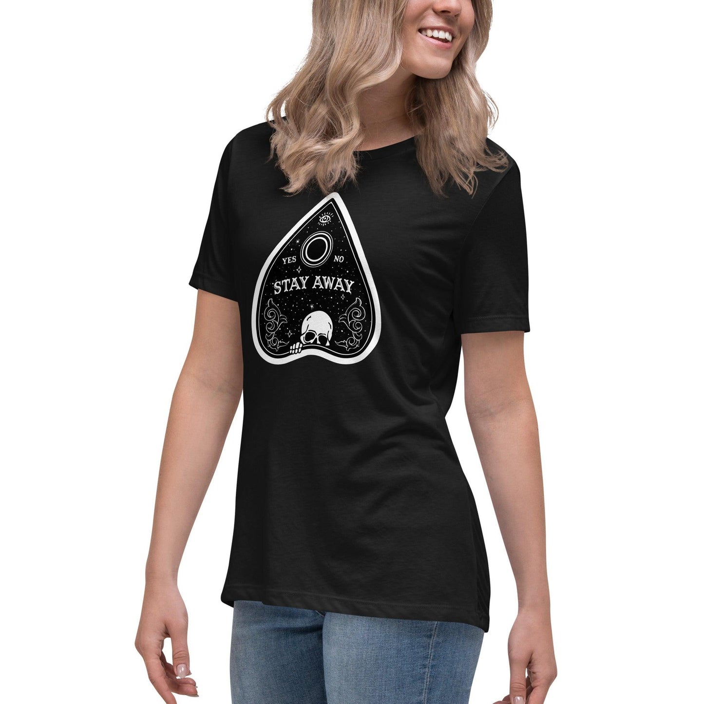 A young woman wearing a black t-shirt with a vibrant Planchette design featuring a skull at the base of the planchette and the evil eye at the top.