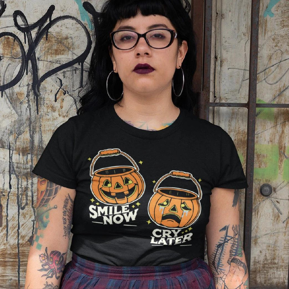 Chicana woman wearing a Halloween-themed t-shirt featuring two jack-o'-lanterns with 'Smile Now, Cry Later' expressions, blending classic Halloween vibes with a Chicano cultural twist.