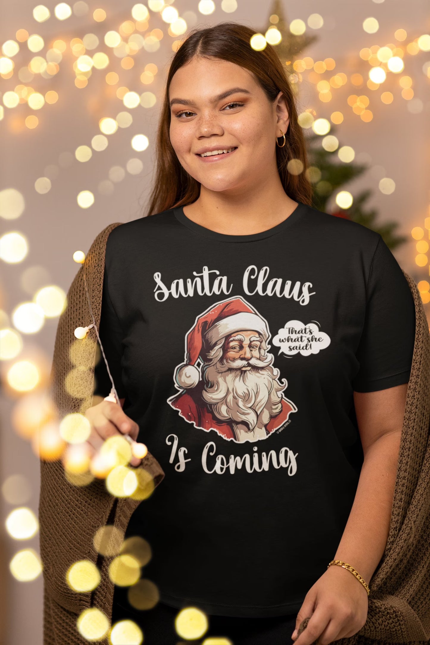 Woman wearing a "Santa Claus Is Coming" unisex shirt with a festive background, highlighting the humorous holiday design.