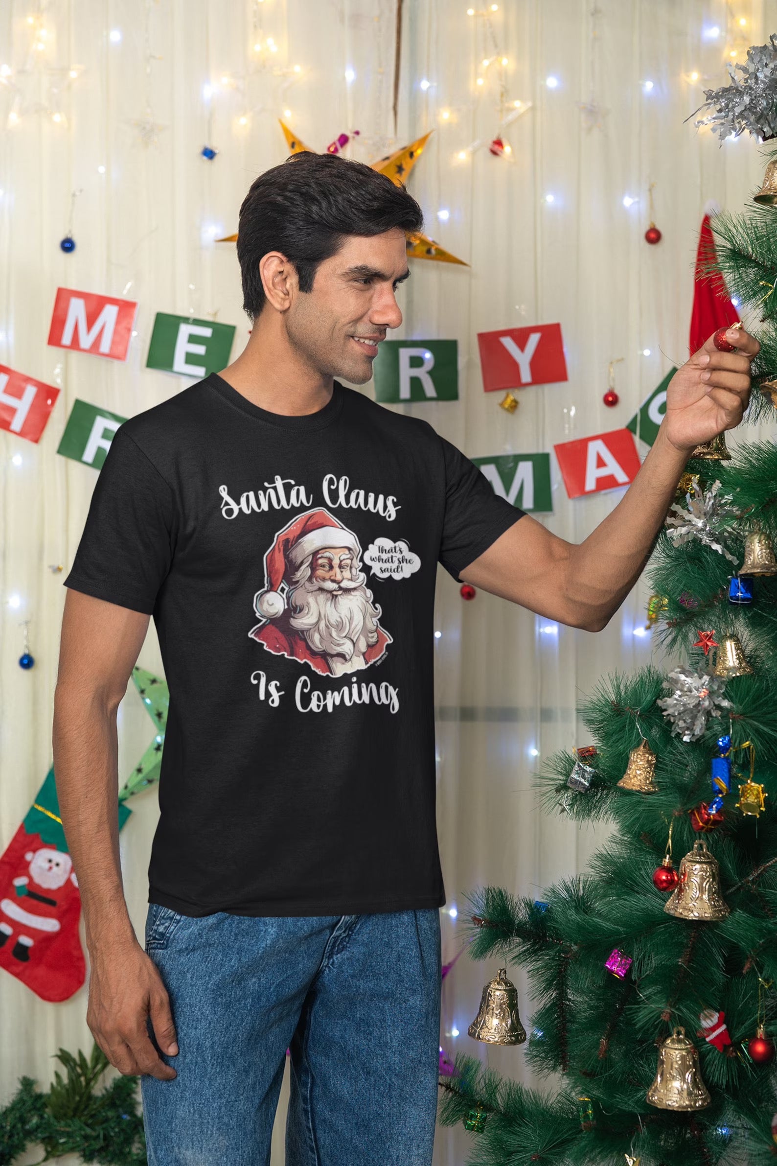 Man decorating a Christmas tree while wearing a "Santa Claus Is Coming" unisex shirt, showcasing the funny and festive graphic.