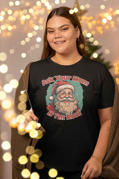 Woman wearing "Ask Your Mom If I'm Real" Unisex Funny Christmas T-Shirt in front of festive lights – Funny Christmas T-Shirt, Sarcastic Holiday Shirt, Santa Claus Tee.