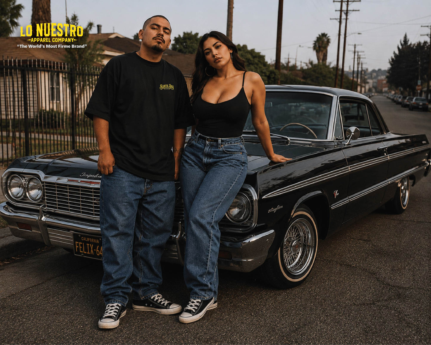 Two models posing with a classic black car on a street, wearing black t-shirts and blue jeans. The image has a warm, golden-hour look and features a yellow logo in the top left corner that reads 'LO NUESTRO APPAREL COMPANY'.