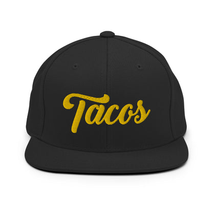 Black snapback hat with "Tacos" text in yellow, featuring a flat bill and adjustable snapback closure.