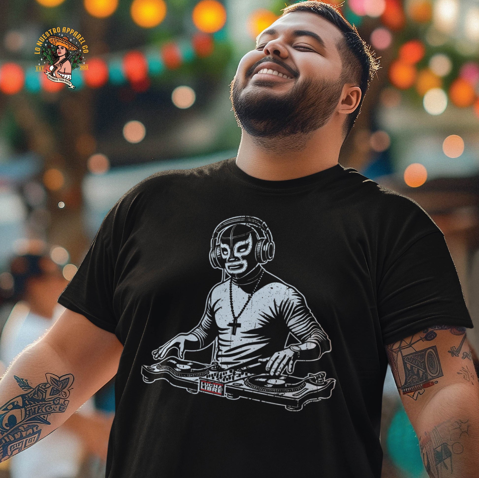 A smiling man wearing the Luchador DJ T-Shirt, a Funny Mexican Shirt that fuses lucha libre and DJ culture. This Chicano clothing piece features a bold design of a masked DJ behind turntables, perfect for music lovers and lucha fans alike.