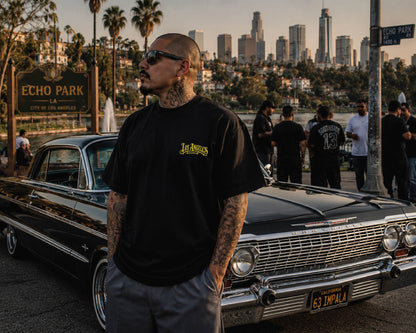 Model wearing the Los Angeles Plaque t-shirt at Echo Park with a black 1963 Impala lowrider in the background featuring the front chest print.