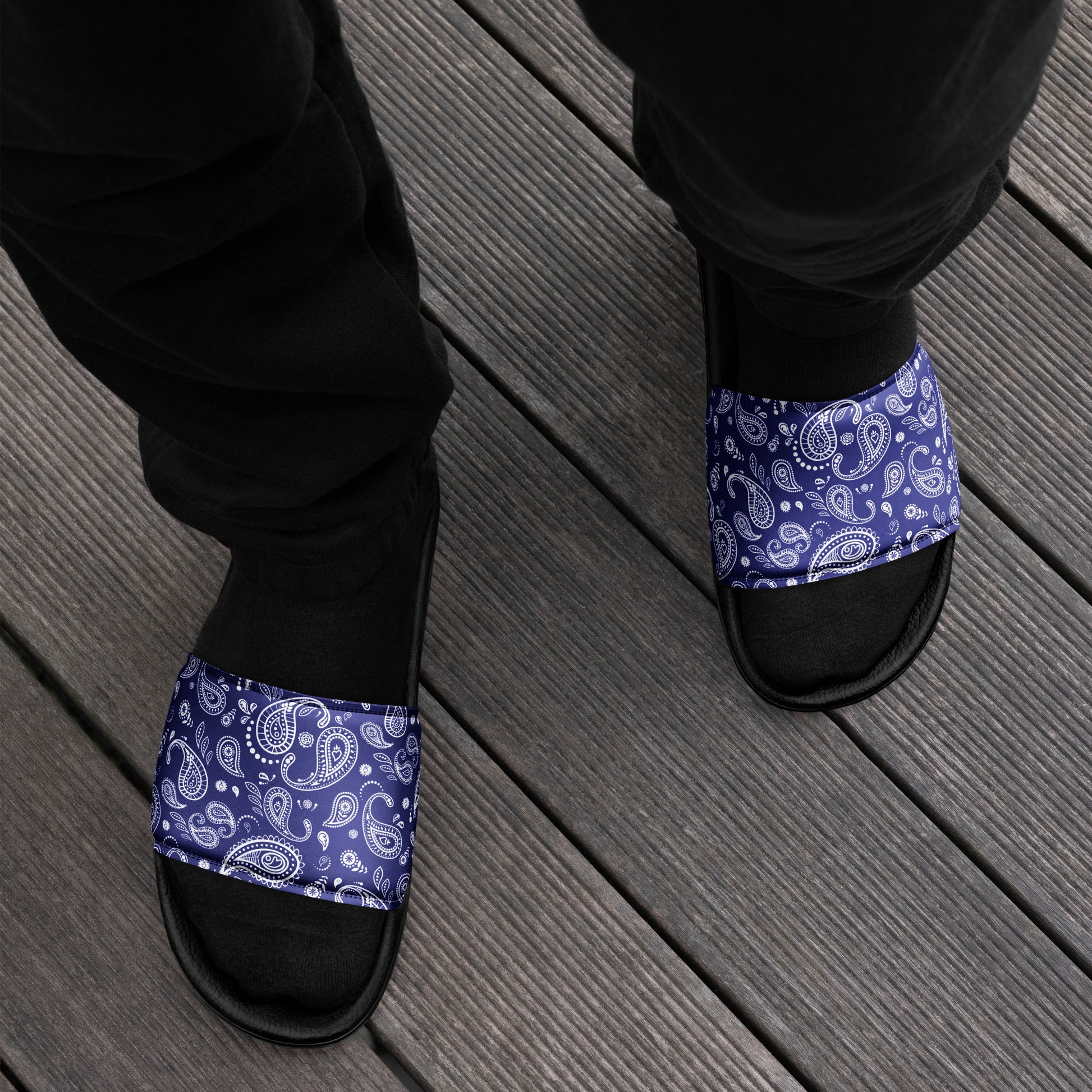 Person lounging on a wooden deck wearing Men's Blue Bandana Slide Sandals, adding a touch of street style to their casual look.