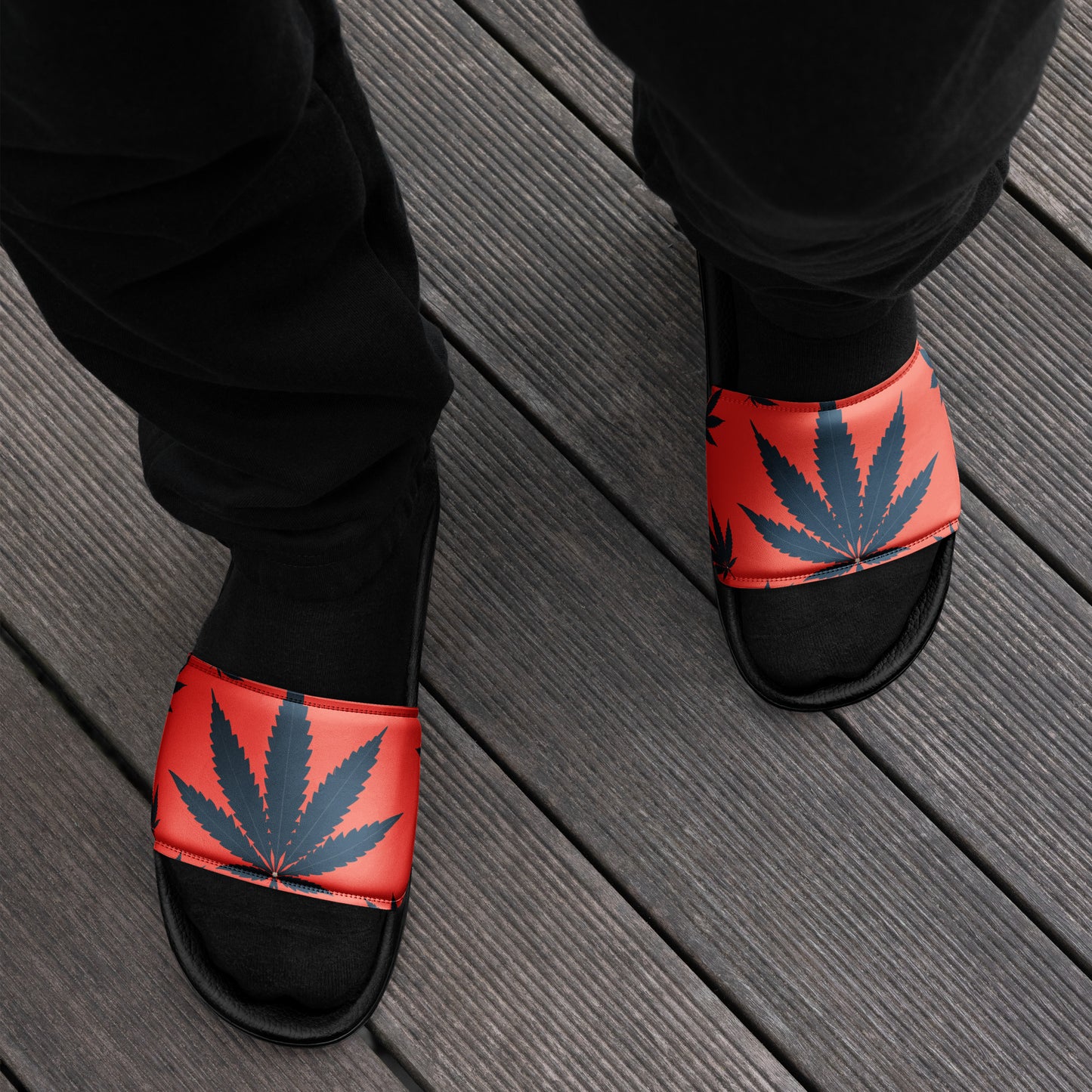 Person wearing Men's Mary Jane Faux Leather Slides with a bold weed leaf design, standing on a wooden deck. The vibrant orange base and blue marijuana leaves make a standout fashion statement.