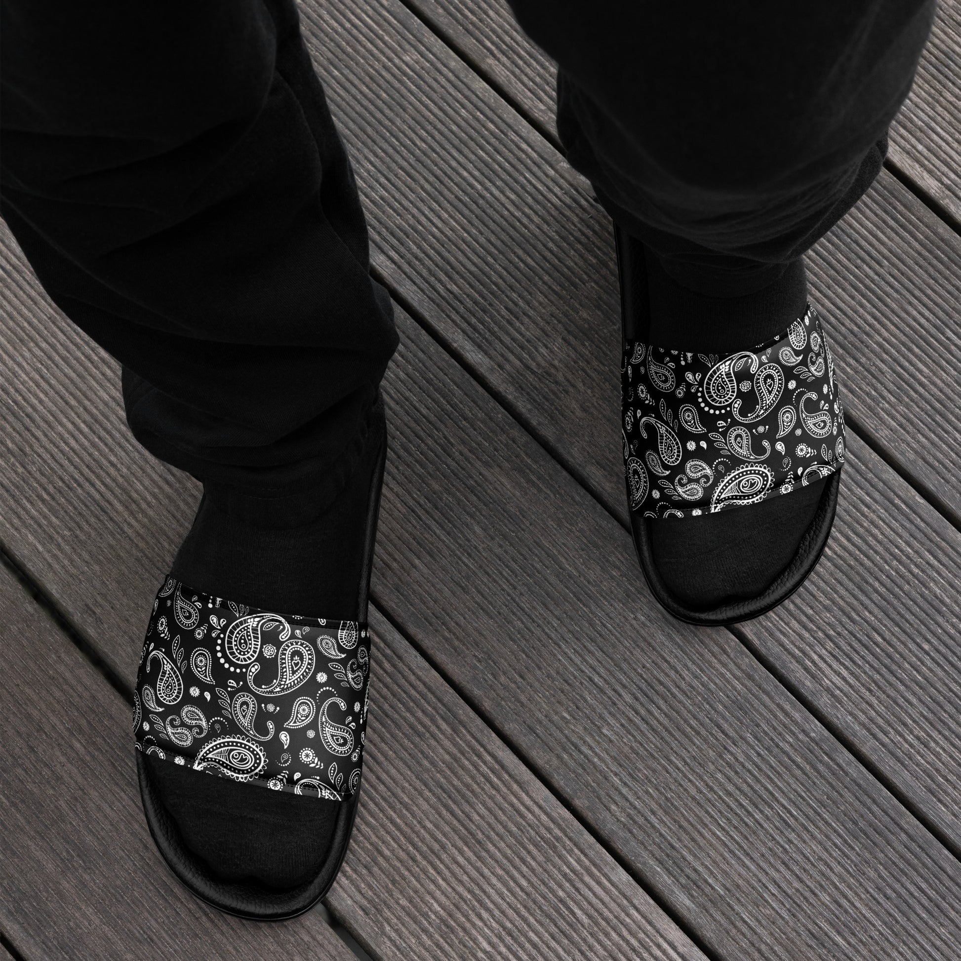 Person lounging on a wooden deck wearing Men's Black Bandana Slide Sandals, adding a touch of street style to their casual look.