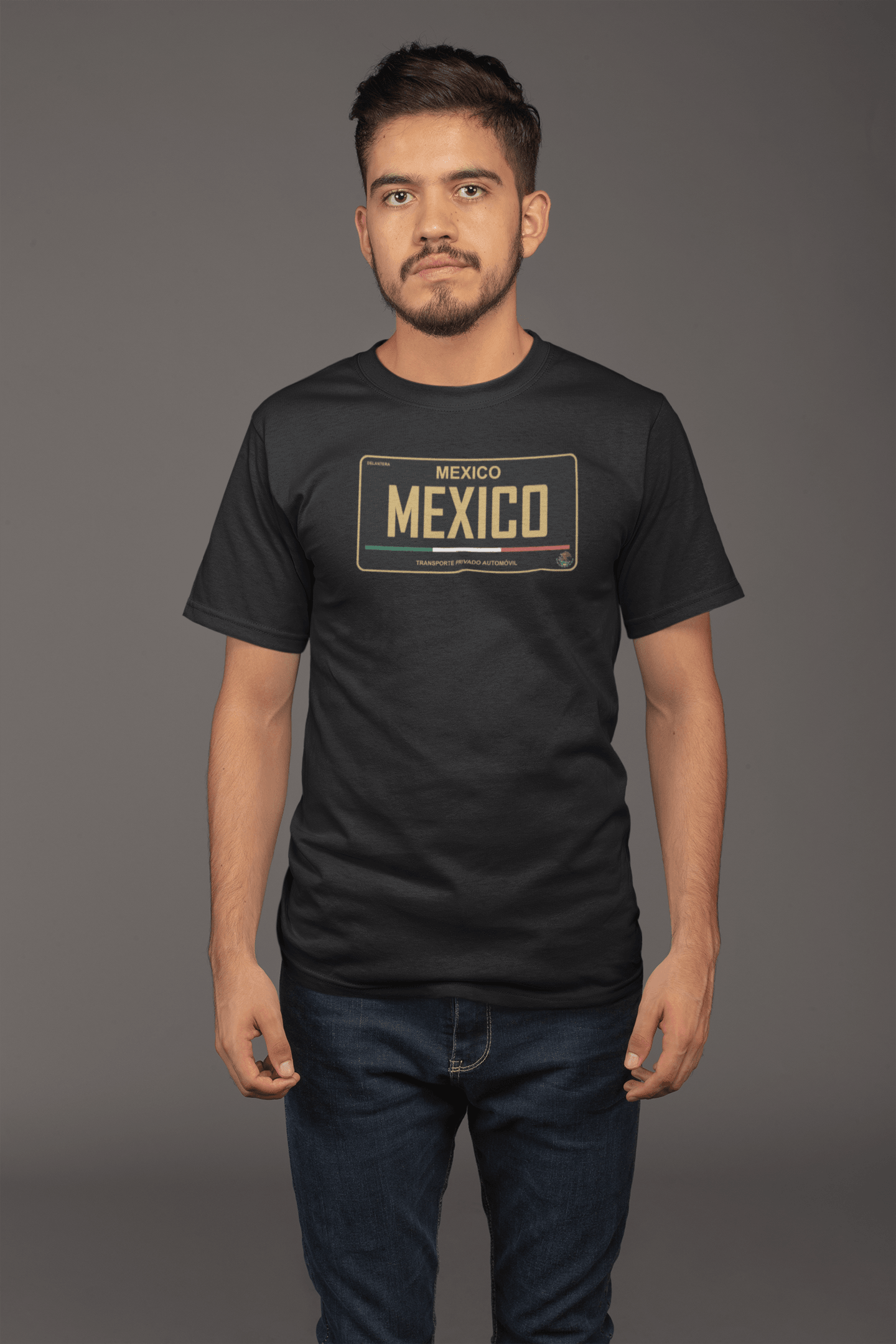 A young man wearing a black t-shirt with a Mexico license plate graphic, showcasing gold lettering and Mexican flag colors, standing against a plain background.