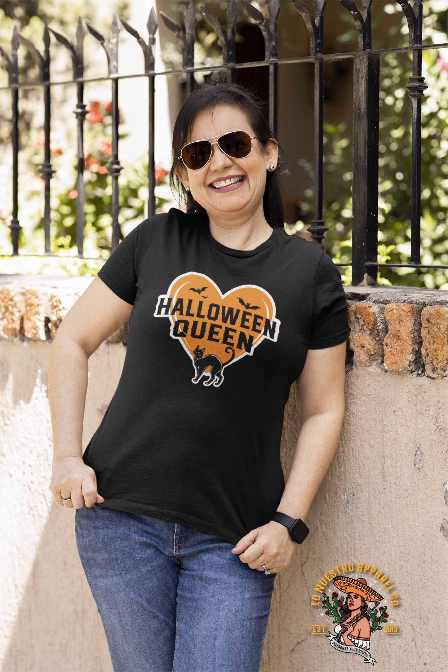 Smiling woman wearing the 'Halloween Queen' Women’s T-Shirt in Black, featuring an orange heart with a black cat and bats, perfect for showing off spooky style.