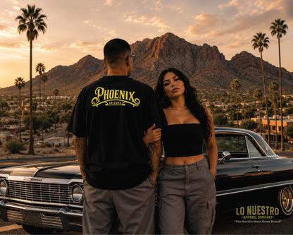 Hispanic couple wearing the Phoenix California plaque T-shirt in front of Camelback Mountain and a classic black 1963 Chevrolet Impala in Phoenix, Arizona.
