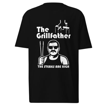 Black t-shirt laid flat on white background featuring The Grillfather design with puppet strings, a cholo-style character holding tongs, and the phrase The Steaks Are High.