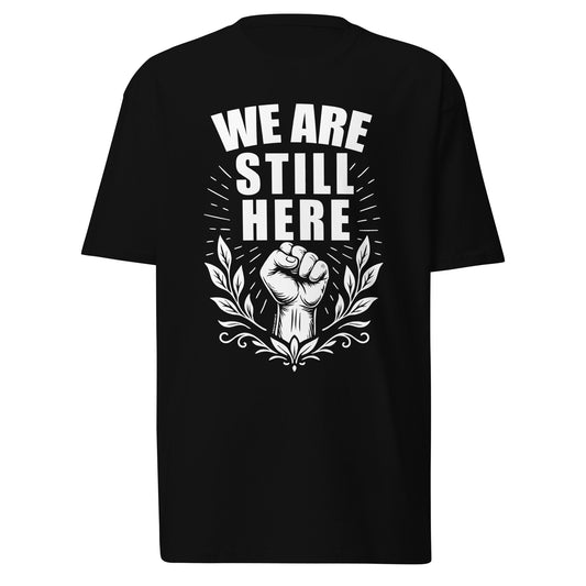 Black We Are Still Here t-shirt displayed on a clean white background, featuring bold white lettering, a raised fist, and floral design for cultural empowerment.