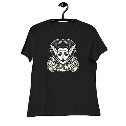 Black women's t-shirt with a retro tattoo-style design of the Bride of Frankenstein, featuring the 'Sad Monster's Club' text in a banner. The shirt is displayed on a hanger against a plain white background.