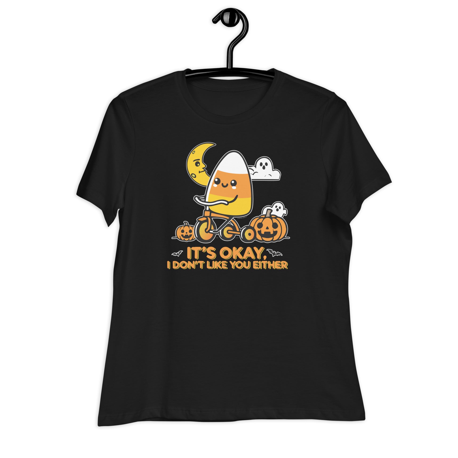 A black t-shirt hung on a hanger featuring a cute candy corn character riding a tricycle. The t-shirt has the Halloween design with pumpkins, a crescent moon, ghosts, and the phrase "It's okay, I don't like you either.