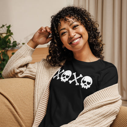 A young woman sitting on a couch wearing a knitted sweater and wearing a black tshirt with the XOXO skull and bones shirt.